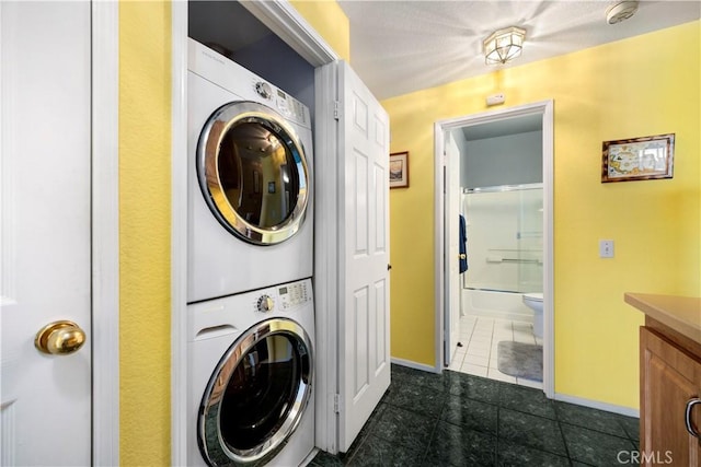 clothes washing area with dark tile patterned flooring and stacked washer and clothes dryer