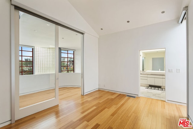 unfurnished bedroom featuring vaulted ceiling, connected bathroom, and hardwood / wood-style floors