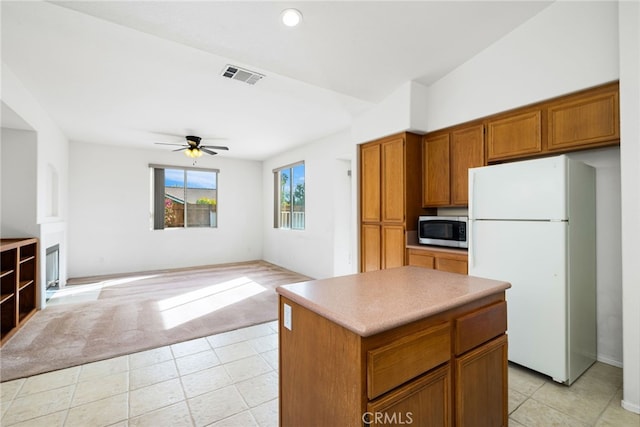 kitchen with ceiling fan, white fridge, a kitchen island, and light carpet