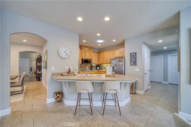 kitchen with a kitchen breakfast bar, sink, light brown cabinetry, kitchen peninsula, and stainless steel appliances