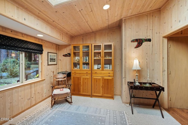 sitting room featuring wood walls, vaulted ceiling with skylight, light hardwood / wood-style floors, and wooden ceiling