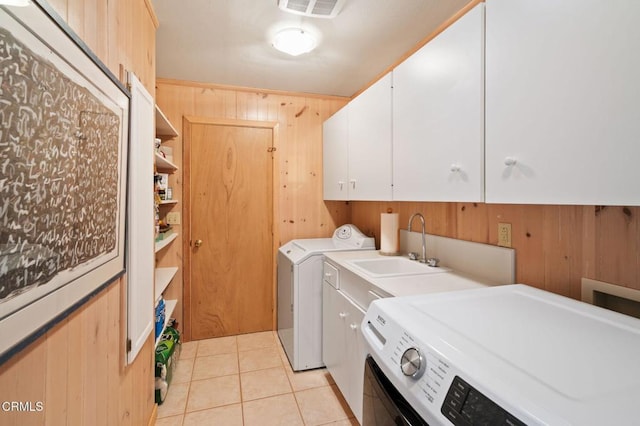 clothes washing area with cabinets, sink, light tile patterned floors, independent washer and dryer, and wood walls