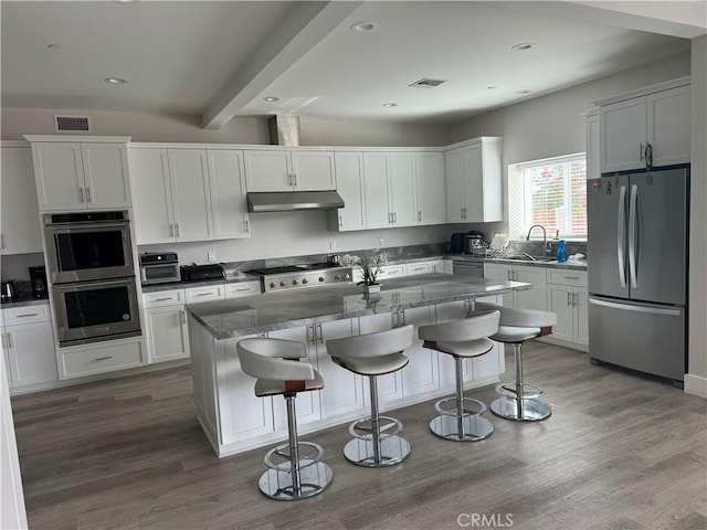 kitchen featuring stainless steel appliances, sink, white cabinetry, hardwood / wood-style flooring, and a kitchen island