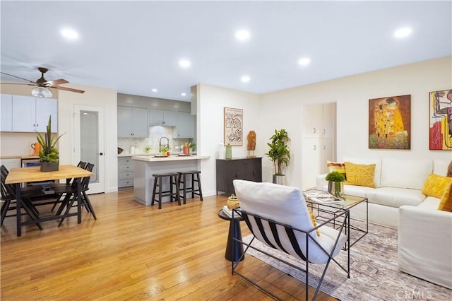 living room featuring ceiling fan, sink, and light hardwood / wood-style flooring