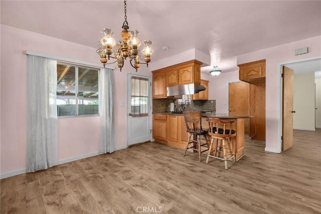 kitchen with a kitchen breakfast bar, light wood-type flooring, backsplash, a chandelier, and hanging light fixtures