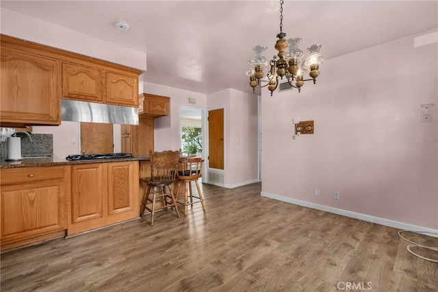 kitchen featuring dark stone counters, stainless steel gas cooktop, pendant lighting, an inviting chandelier, and hardwood / wood-style floors