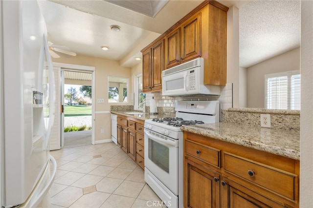 kitchen with ceiling fan, tasteful backsplash, white appliances, a textured ceiling, and light stone counters