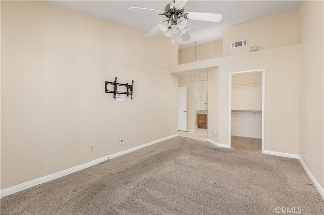 carpeted empty room featuring ceiling fan and a high ceiling