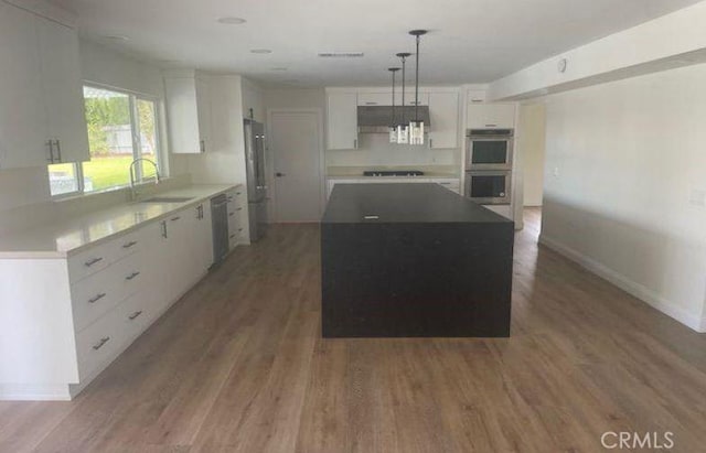 kitchen featuring stainless steel appliances, a kitchen island, sink, white cabinetry, and hanging light fixtures