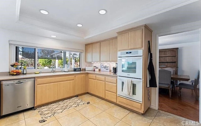 kitchen with light brown cabinets, sink, a raised ceiling, stainless steel dishwasher, and double oven