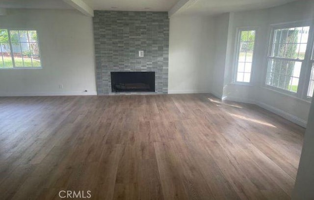 unfurnished living room with a wealth of natural light, a fireplace, beamed ceiling, and wood-type flooring