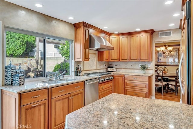 kitchen featuring light stone counters, stainless steel appliances, wall chimney range hood, sink, and an inviting chandelier