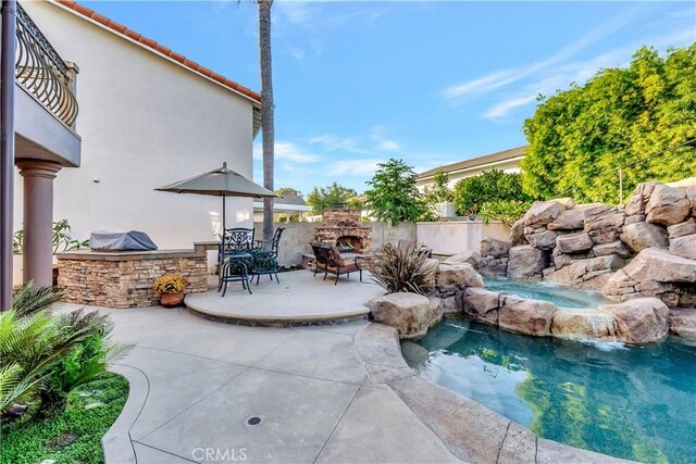 view of pool with pool water feature, an outdoor stone fireplace, a grill, and a patio