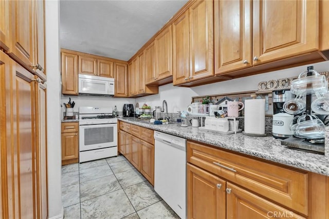 kitchen featuring light stone counters, white appliances, and sink