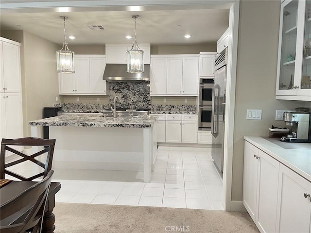 kitchen with light carpet, white cabinetry, hanging light fixtures, and an island with sink