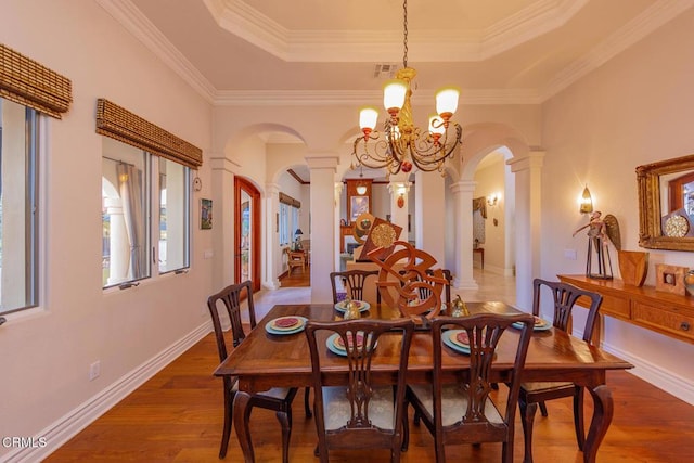 dining room with decorative columns, ornamental molding, a raised ceiling, dark wood-type flooring, and a chandelier