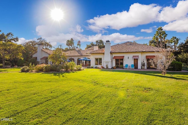 back of property with a lawn, a tile roof, and stucco siding