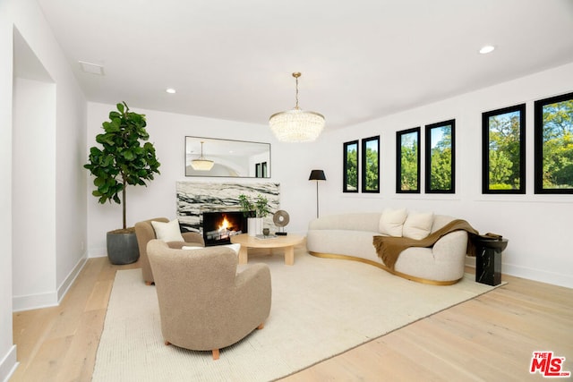 living room with a notable chandelier, light hardwood / wood-style floors, and a premium fireplace