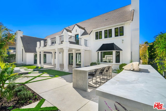 rear view of house with a balcony, exterior bar, and a patio