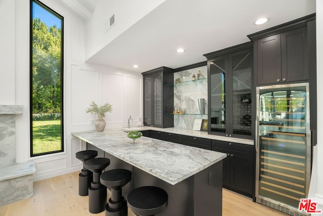 bar with light wood-type flooring, wine cooler, and light stone counters