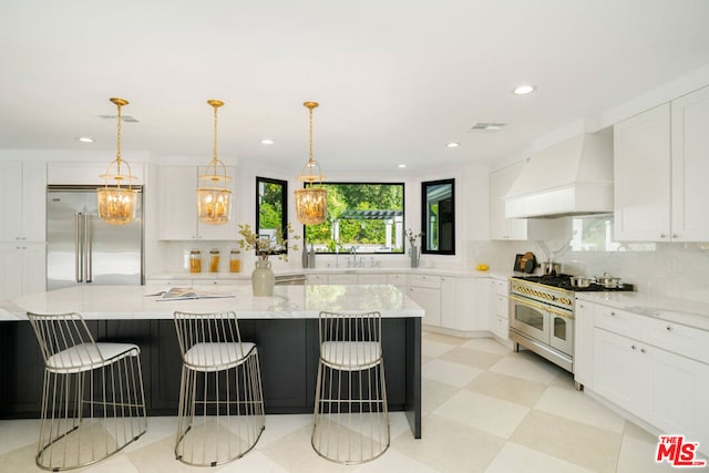 kitchen with custom exhaust hood, a breakfast bar, premium appliances, a spacious island, and white cabinets