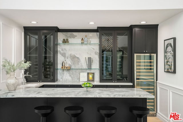 bar with light stone countertops, decorative backsplash, wine cooler, and sink