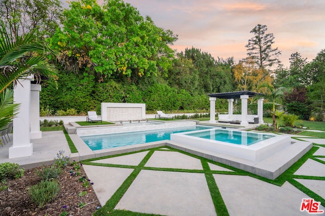 pool at dusk featuring an in ground hot tub and a patio area