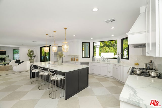 kitchen with a kitchen island, light stone counters, premium range hood, pendant lighting, and white cabinets