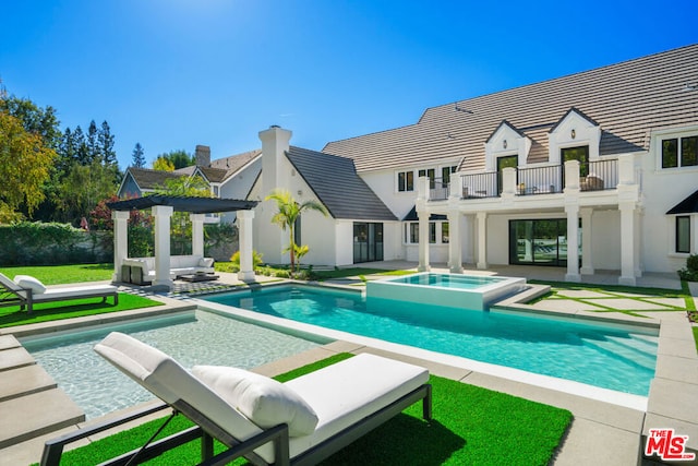 back of house featuring a swimming pool with hot tub, a balcony, and a patio area