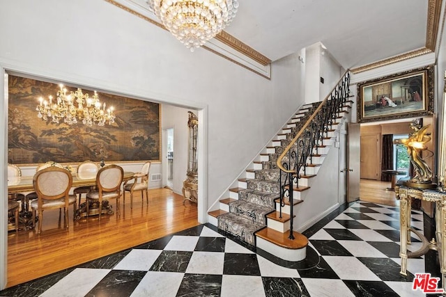 stairs with hardwood / wood-style flooring, a notable chandelier, ornamental molding, and a high ceiling