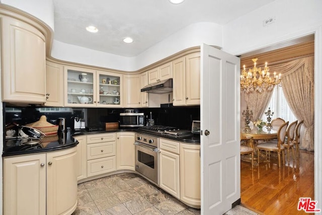 kitchen with backsplash, cream cabinetry, light hardwood / wood-style floors, stainless steel appliances, and a chandelier