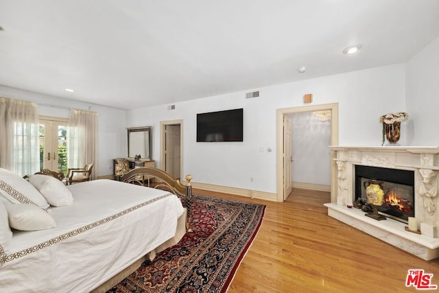 bedroom featuring french doors, light wood-type flooring, and a premium fireplace