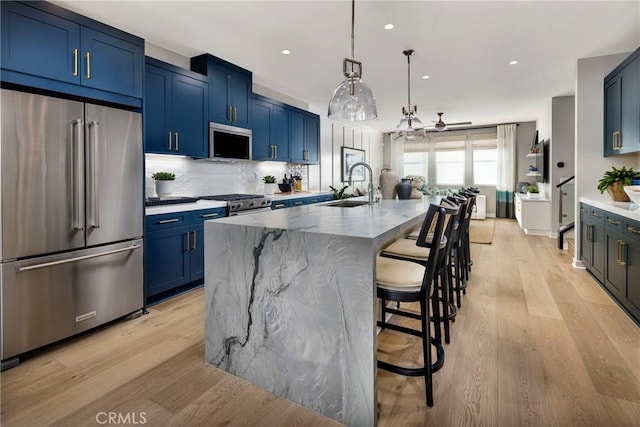 kitchen featuring a center island with sink, sink, ceiling fan, appliances with stainless steel finishes, and a breakfast bar area