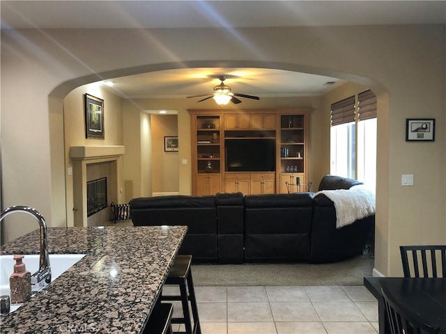 living room featuring ornamental molding, ceiling fan, sink, light tile patterned floors, and a fireplace