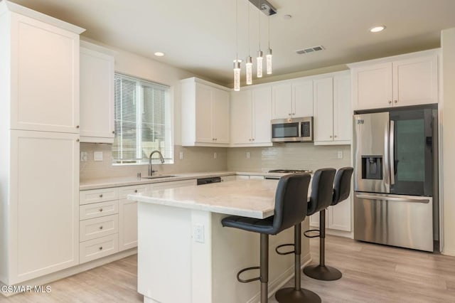 kitchen with sink, a kitchen island, light hardwood / wood-style floors, white cabinets, and appliances with stainless steel finishes