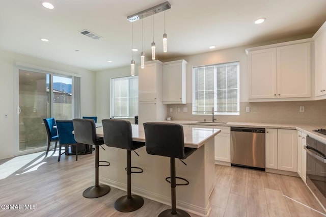 kitchen with sink, hanging light fixtures, stainless steel appliances, white cabinets, and light wood-type flooring