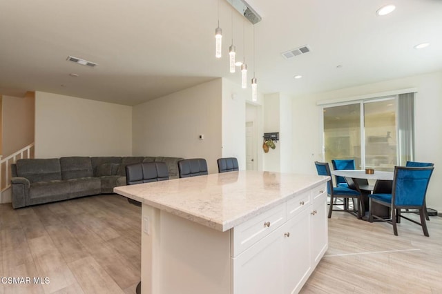 kitchen with a center island, decorative light fixtures, white cabinetry, and light hardwood / wood-style floors