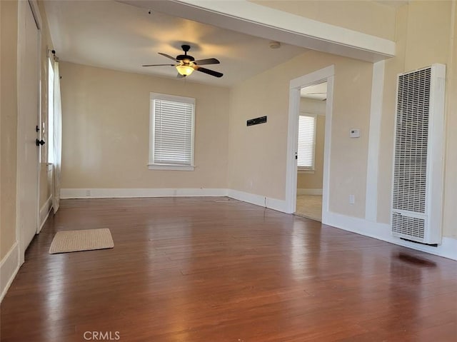 empty room with a heating unit, ceiling fan, baseboards, and wood finished floors