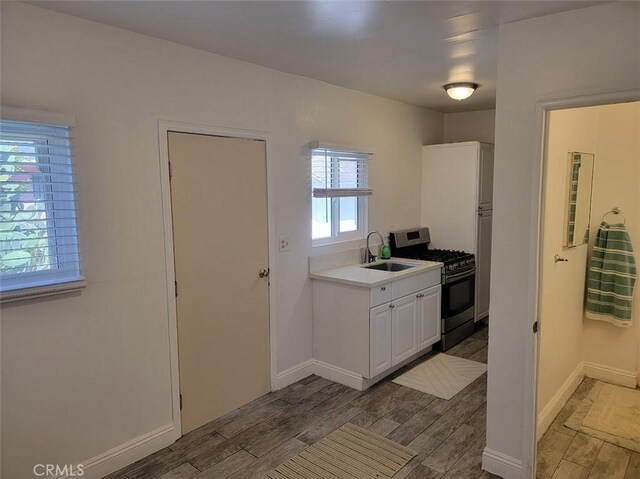 kitchen with light countertops, gas stove, white cabinets, a sink, and wood finished floors