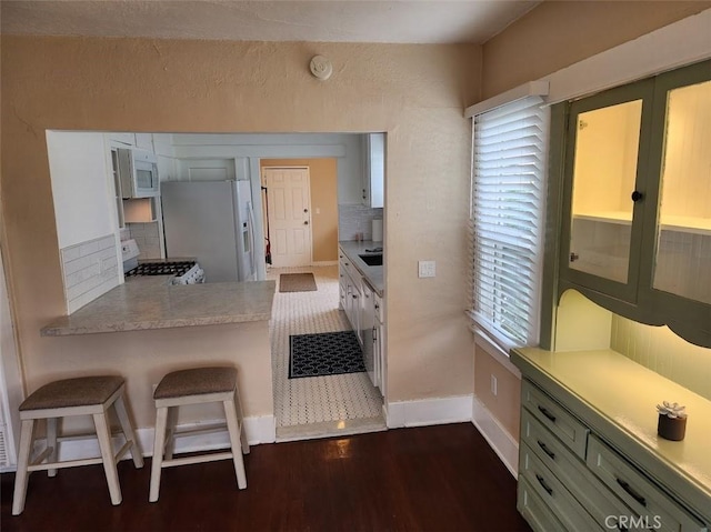 kitchen with white appliances, decorative backsplash, dark wood-style flooring, light countertops, and a kitchen bar