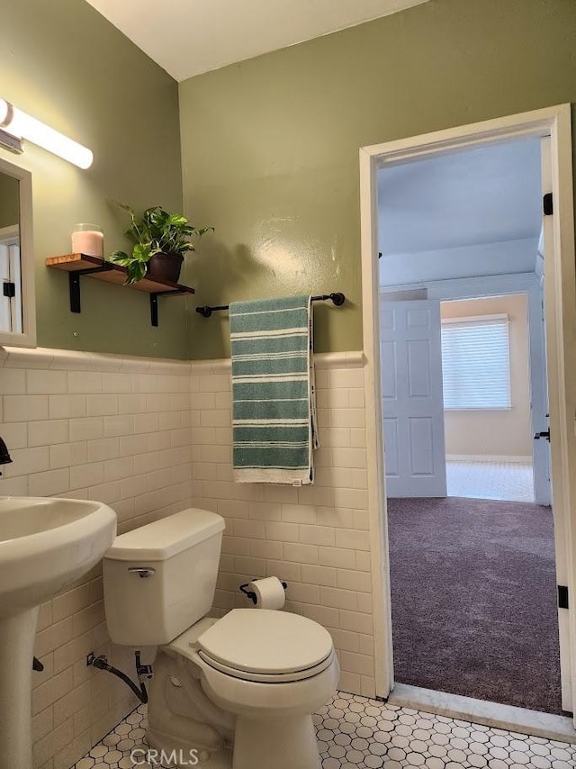 half bathroom featuring wainscoting, toilet, and tile walls