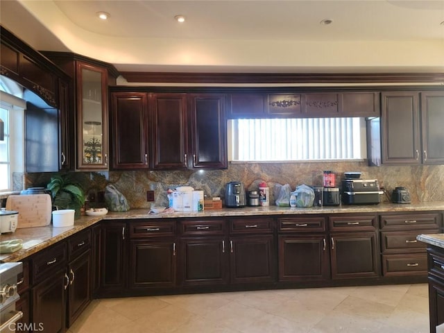 kitchen with tasteful backsplash, light stone counters, dark brown cabinets, and stove