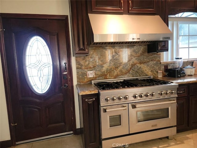 kitchen featuring range with two ovens, exhaust hood, light tile patterned floors, and decorative backsplash