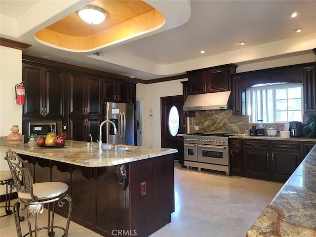 kitchen with a breakfast bar, stainless steel appliances, tasteful backsplash, light stone countertops, and a raised ceiling