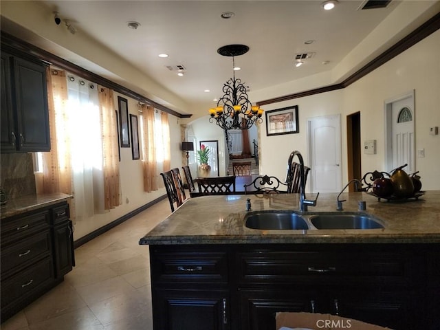 kitchen with sink, a breakfast bar area, hanging light fixtures, a center island with sink, and dark stone counters