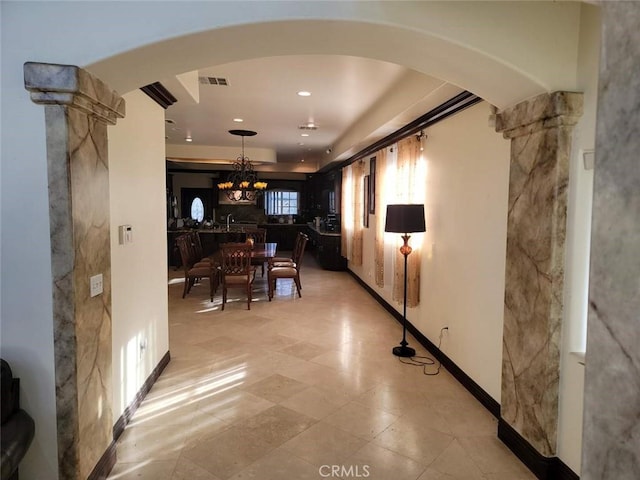 hallway featuring ornate columns and a chandelier