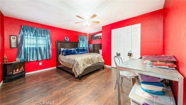 bedroom featuring ceiling fan, a wood stove, dark wood-type flooring, and a closet