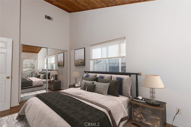 bedroom with hardwood / wood-style flooring, wood ceiling, a towering ceiling, and a closet