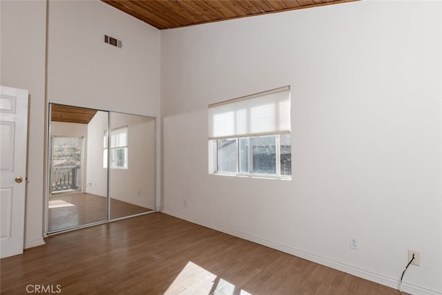 unfurnished bedroom featuring a high ceiling, dark hardwood / wood-style floors, a closet, and wooden ceiling