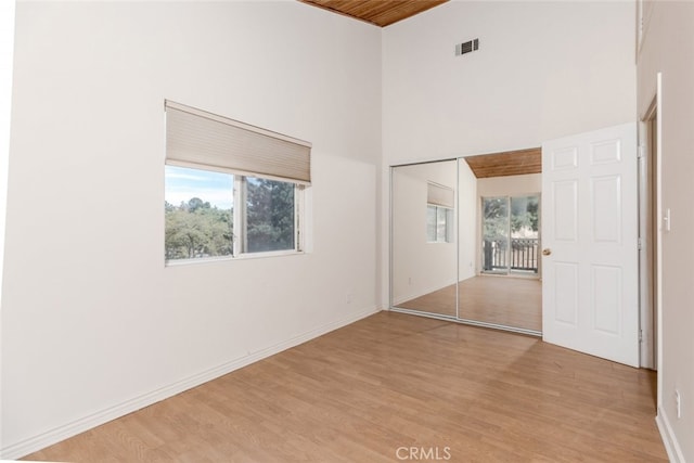 unfurnished bedroom with a high ceiling, light wood-type flooring, a closet, and multiple windows